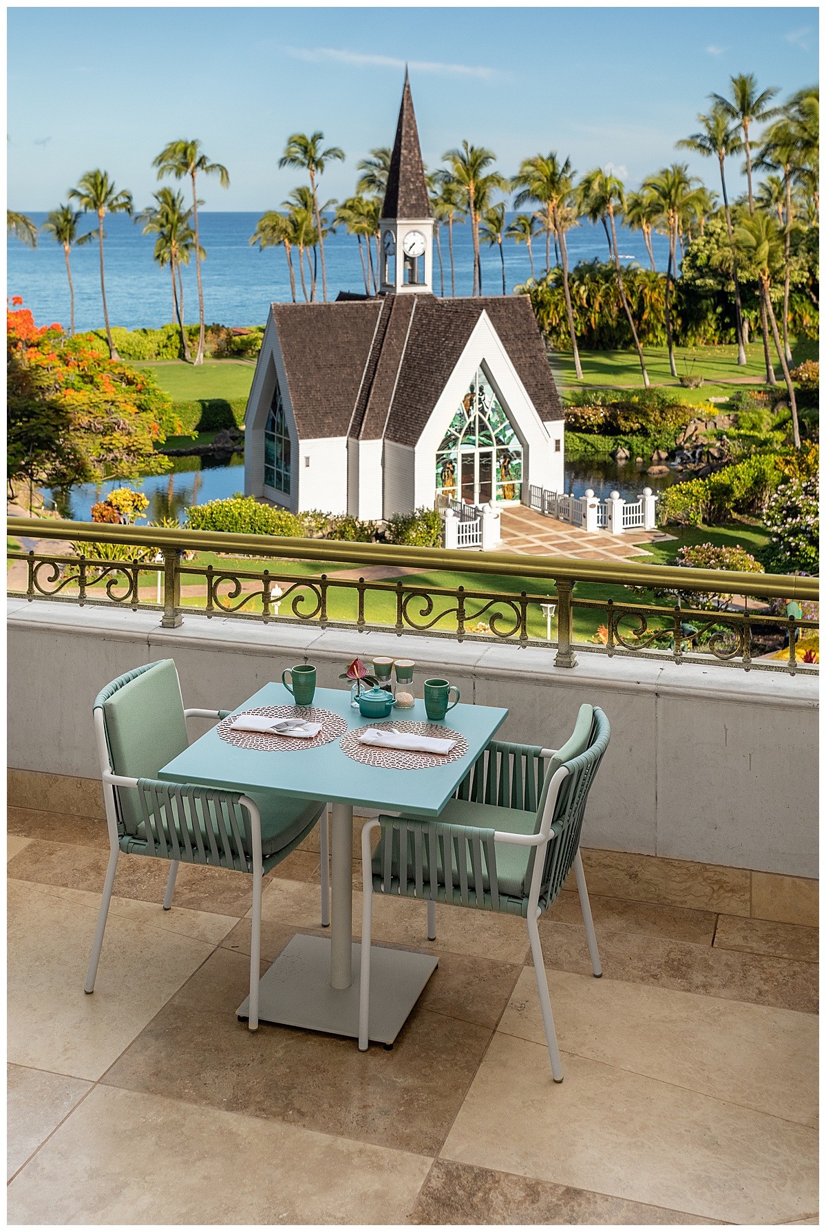 A view from one of the tables at the restaurant. The table and chairs are teal. The table looks over the railing at the resort's wedding chapel, green lawn, and blue ocean.