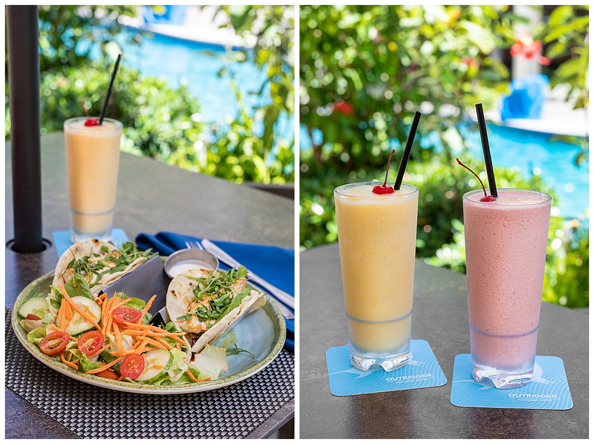 Lunch and smoothies at the poolside bar. The lunch is fish tacos with a side salad. The smoothes are a yellow mango and a pink strawberry. They are both in tall glasses with black straws and cherries. The pool is out of focus in the background.